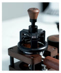 Heavy Duty 58 Millimeter Espresso Portafilter Needle Distributor With Built In Magnet resting on wood base with brown handle.