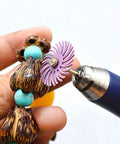Close-up of blue rotary tool with purple radial bristle disc polishing wheel against turquoise and wooden beads.