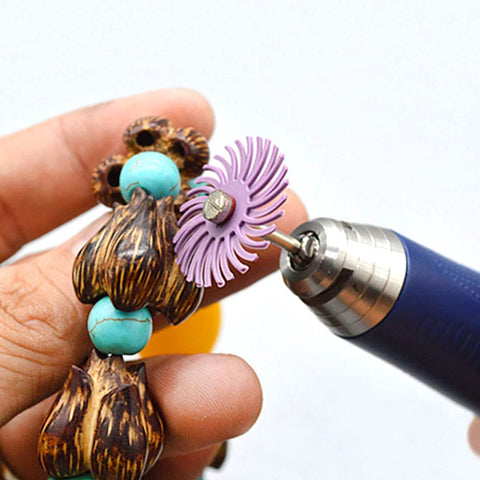 Close-up of blue rotary tool with purple radial bristle disc polishing wheel against turquoise and wooden beads.