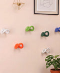 Set of Six Playful Ceramic Wall Hooks for Coats and Keys Game Changer Storage Solution in assorted colors on a wall with plants.