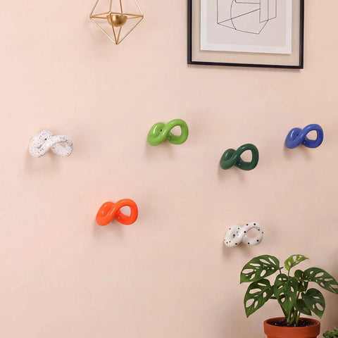 Set of Six Playful Ceramic Wall Hooks for Coats and Keys Game Changer Storage Solution in assorted colors on a wall with plants.
