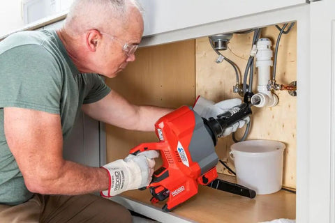 Man using Heavy Duty Cordless Drain Snake With Brushless Motor and Twenty Five Foot Steel Cable for clogs under sink.