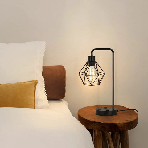 Industrial Dual USB Desk Lamp with Edison Style Bulb in Black Metal Cage on Wooden Nightstand in Bedroom.