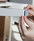 Person applying self adhesive furniture sliders for carpet hardwood and tile floors with 30mm chair leg glides on a chair leg.