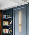 Slick Modern Wall Sconce Light Fixture Offering Three Color Temperatures And Built In Led Bulbs, mounted on dark wall near bookshelves.