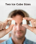 Two bullet ice cubes held between fingers in close-up, clear white ice.