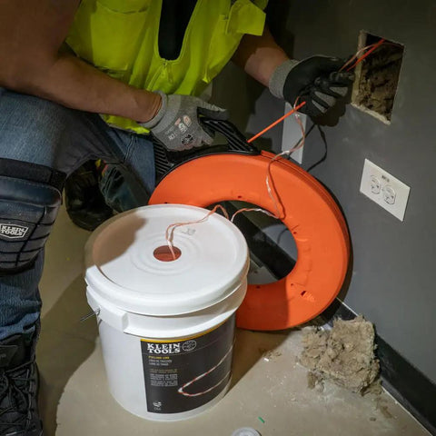 Worker using Poly Pull Line For Wire Pulling, Orange Tracer Cord from a reel for light duty cable string, high visibility orange and white.