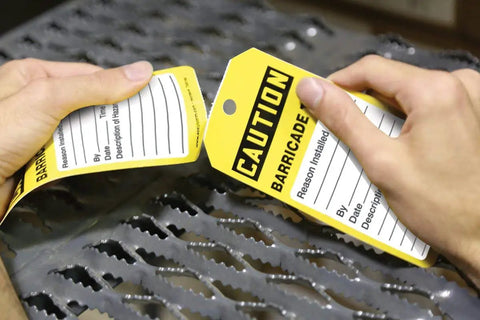 Hands tearing NMC 100 Safety Tags By The Roll Caution Barricade OSHA Compliant Waterproof PF Cardstock Tags