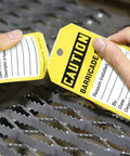 Hands tearing a Safety Tags By The Roll Caution Barricade OSHA Compliant Waterproof PF Cardstock Tear Resistant tag