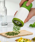 Cilantro And Spice Grinder Manual Stainless Steel Green Easy Clean Kitchen Tool grinding herbs onto a wooden cutting board