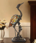 Crane Bird Stained Glass Table Lamp With Resin Accents, Retro Vintage LED Desk Light, brass finish, next to a vase of flowers.