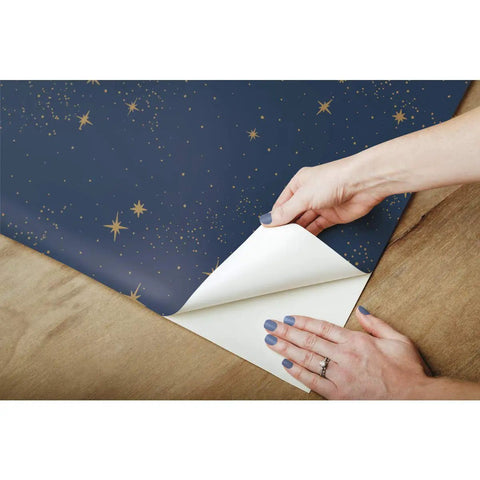 Hands applying Upon A Star Navy And Metallic Peel And Stick Wallpaper For A Quick No Mess Makeover Great For Renters And Homeowners