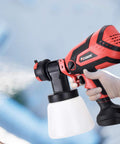 Hand holding a Powerful HVLP Paint Sprayer With 750W Motor And 4 Nozzles, 1000ml Cup for Home And Outdoor Projects in bright red.