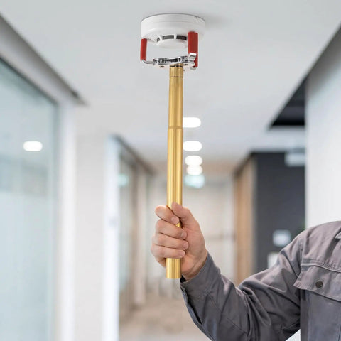 Ladder Free Smoke Transducer Assembly Tool With Heavy Hitter Sensor Head For High Ceiling Detectors, holding gold extension bar.