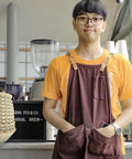 Barista wearing orange shirt and brown apron in a cafe with Hella Durable Unbleached Brown Biodegradable Coffee Filters.
