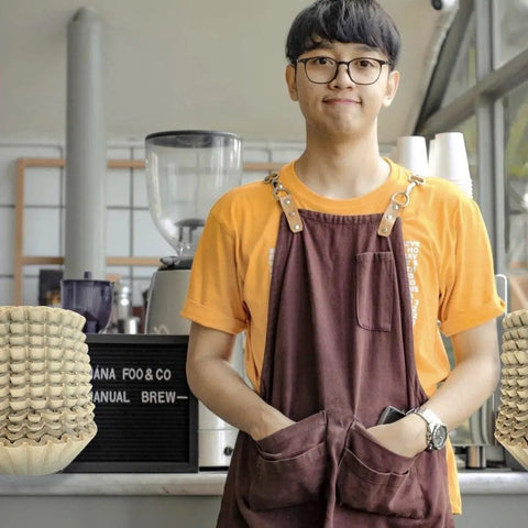 Barista wearing orange shirt and brown apron in a cafe with Hella Durable Unbleached Brown Biodegradable Coffee Filters.