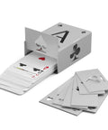 Deck of playing cards partially pulled from a silver card dispenser, with additional cards scattered beside it.