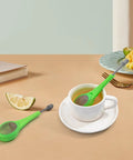 Long Handled Tea Infuser With Fine Mesh Strainer And Built In Plunger Reusable Loose Leaf Coffee Filter Dual Compartment Spice Steeper For Rich Aroma And A Smooth Sip Every Time Green resting in a white cup of tea.