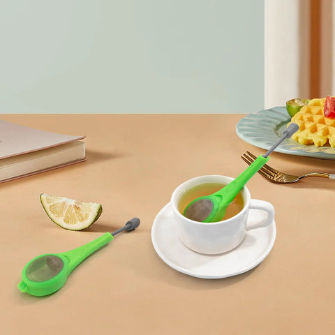 Long Handled Tea Infuser With Fine Mesh Strainer And Built In Plunger Reusable Loose Leaf Coffee Filter Dual Compartment Spice Steeper For Rich Aroma And A Smooth Sip Every Time Green resting in a white cup of tea.