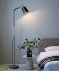 Three Color Temperature Floor Lamp With Adjustable Head And Energy Efficient Nine Watt LED Bulb Included For Living Room Bedroom Office Farmhouse Modern Standing Task Lighting For A Cozy Vibe next to a bed with a side table and plant.