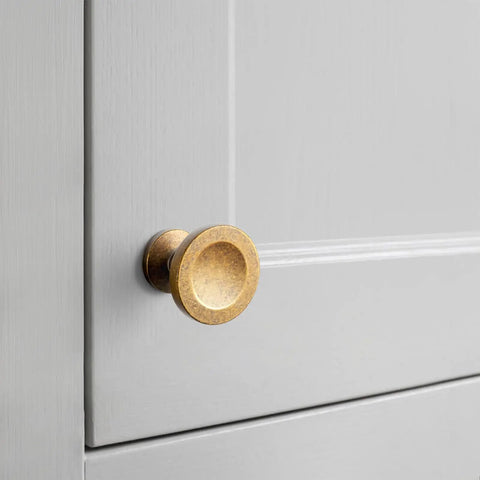 Close-up of 12 Pack Antique Brass Round Cabinet Knobs With Single Hole on a gray cabinet door