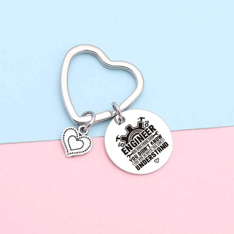 Heart-shaped stainless steel keychain on pastel background with engraved 'Engineer' text for Engineering Student Gift Keychain For Graduation Cool Mechanical Engineer Jewelry For Coworkers And Students Software And Hardware Nerds Will Love Engraved Stainless Steel Gift For Engineering School Grad.