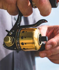 Close-up of Underspin Spincast Reel For Freshwater Fishing Dope Ambidextrous Handle One Ball Bearing 4.1 To 1 Gear, gold finish in use.
