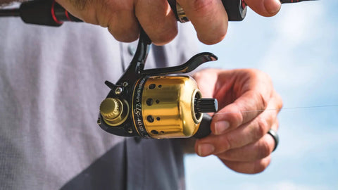 Close-up of Underspin Spincast Reel For Freshwater Fishing Dope Ambidextrous Handle One Ball Bearing 4.1 To 1 Gear, gold finish in use.