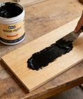 Applying Deep Black Wood Filler And Putty 9.87oz For Furniture Repair Kit on wood surface with a scraper, showing its usage.