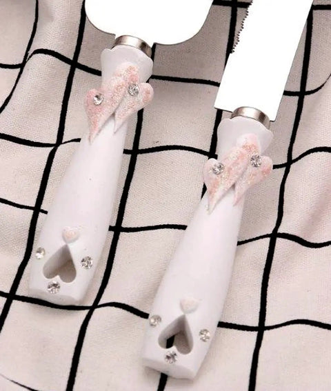 Close-up of handles on a Personalized Rose Gold Wedding Cake Knife And Server Set With Double Heart Engraving on checkered cloth.