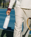 Person holding a Top Tier Insulated Stainless Steel Water Bottle 32 Oz With Chill FreeSip Dual Drink Modes on a tennis court.