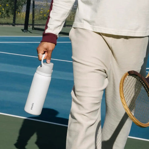 Person holding a Top Tier Insulated Stainless Steel Water Bottle 32 Oz With Chill FreeSip Dual Drink Modes on a tennis court.