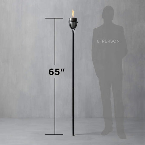 65 Inch Outdoor Torch With Amped Up Extra Large Flame For Patio Garden Lawn And Backyard Weather Resistant Refillable And Decorative Torch In Silver Finish Twist And Pour Refilling For Mess Free Fueling next to 6-foot person for scale.