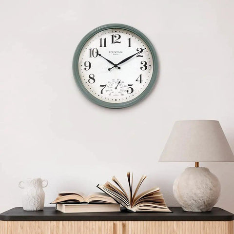 Cool Outdoor And Indoor Weather Station Clock With Thermometer Fahrenheit And Celsius Analog Two In One Wall Decor In Aged Teal Finish 13 Inch Perfect For Patio Porch Garden Kitchen Or Office Wall Mount displayed indoors above a table with books and a lamp.