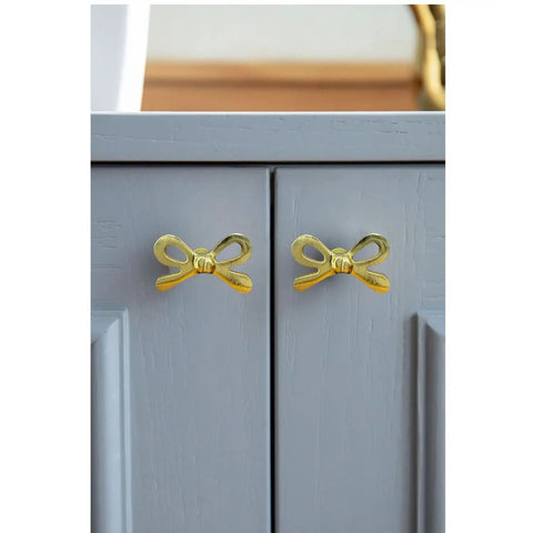 Set Of 8 Brass Bow Knobs For Cabinets And Drawers installed on a grey cabinet, Decorative Bow Hardware For Kitchen Cupboards