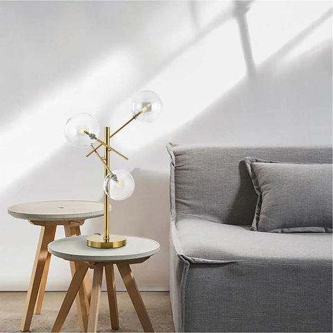 Modern Gold Table Lamp With 3 Light Glass Globe Bulbs, Antique Brass Finish, on a side table in a stylish living room setting.