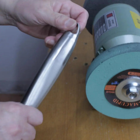 Hand holding a polished stainless steel piece next to a bench grinder, showcasing Six Inch Elastic Polyurethane Buffing Wheel Two Thousand Grit Yields Ridiculously Smooth Mirror Polish On Stainless Steel And Copper With Three Quarter Inch Arbor Knockout Addition To Your Bench Grinder Setup.