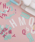 Number Shaped Die Cut Set, 0 Through 9, scattered letters and numbers next to a die cutting machine on a pink background