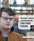 Top Tier Frameless Safety Glasses With Anti Fog Smoke Lenses And Scratch Resistant Coating For Super Comfy All Day Wear Plus Hella Tough Ansi High Impact Eye Protection For Men And Women In Sweet Value Packs Of Twelve worn by a man outdoors.