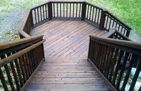 Top Shelf Heavy Duty Oil Based Wood Stain For Exterior Decks Fences Siding Logs Featuring Knockout UV Shielding And Deep Soak Water Repellent Formula In Easy Roll Semi Transparent Rustic Brown Covers Large Patios on a wooden deck with railings.