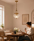 Straight Up Vintage Vibes Handblown Textured Glass Pendant Light With Brushed Antique Brass Finish illuminating a dining table.