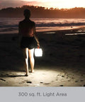 Person walking on beach with Two In One Solar Camping Lantern And Phone Charger For Trail Ready Outdoor Adventures LED light at dusk.
