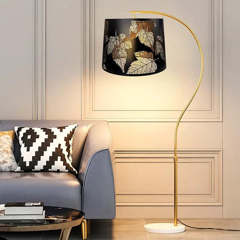 Living room setup with metal etched drum lamp shade with dope leaf pattern for table and floor lamps large 12 by 14 by 10 inch spider fitter harp required alucset metal construction durable aluminum finish. Floor lamp with gold stem and black shade featuring leaf design.