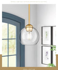 Gold Finish Industrial Pendant Light With Clear Glass Globe Shade in modern interior setting with window and wall art