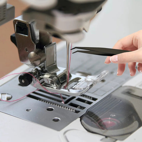 Front view of a sewing machine with a hand holding black tweezers near the needle plate and presser foot.