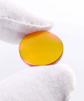 Close-up of a 20mm CO2 laser lens, 50.8mm focal length, ZnSe PVD-coated, orange-yellow tint, held by a gloved hand