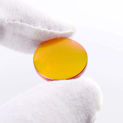 Close-up of a 20mm CO2 laser lens, 50.8mm focal length, ZnSe PVD-coated, orange-yellow tint, held by a gloved hand
