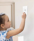 Child reaching for a light switch with clear toggle switch plate guard installed for safety. Clear Toggle Switch Plate Guards 10 Pack for Indoor and Outdoor Wall Plates Keeps Switches From Getting Flipped On Or Off and Adds Kid Safe Security For Everyday Home Safety.