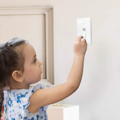 Child reaching for a light switch with clear toggle switch plate guard installed for safety. Clear Toggle Switch Plate Guards 10 Pack for Indoor and Outdoor Wall Plates Keeps Switches From Getting Flipped On Or Off and Adds Kid Safe Security For Everyday Home Safety.