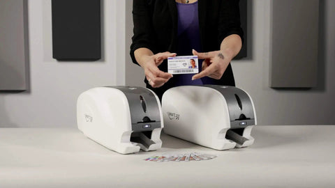 Smart-31 Simplex Id Card Printer Bundle With No Sweat Ezload Kit And Windows Software Includes Two Hundred Fifty Ymcko Ribbon Plus One Hundred Top Shelf Pvc Cards Straight Out The Box with a hand holding a printed ID card.